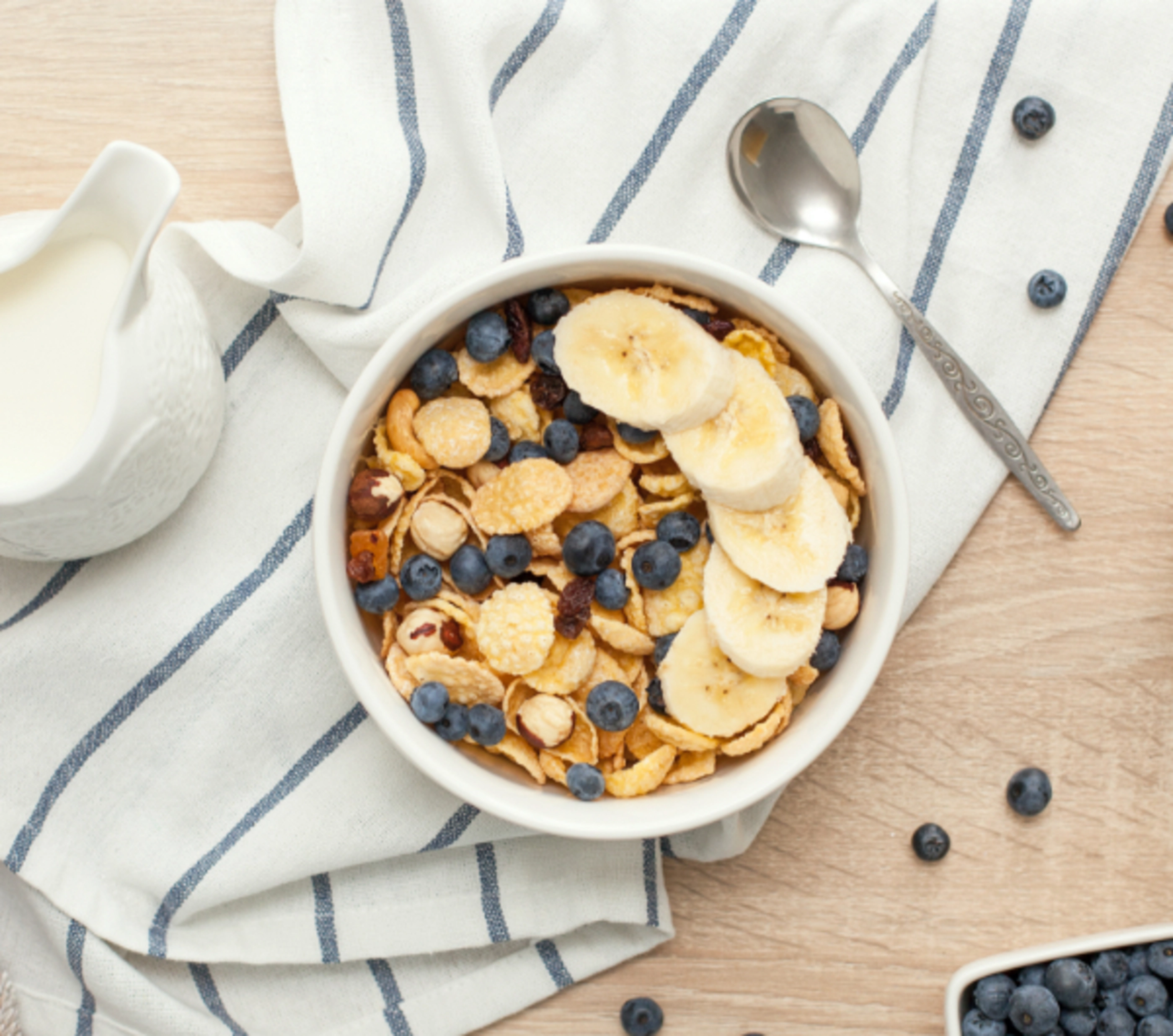 A bowl of bran cereal covered in blueberries and bananas on top of a white and blue striped towel.