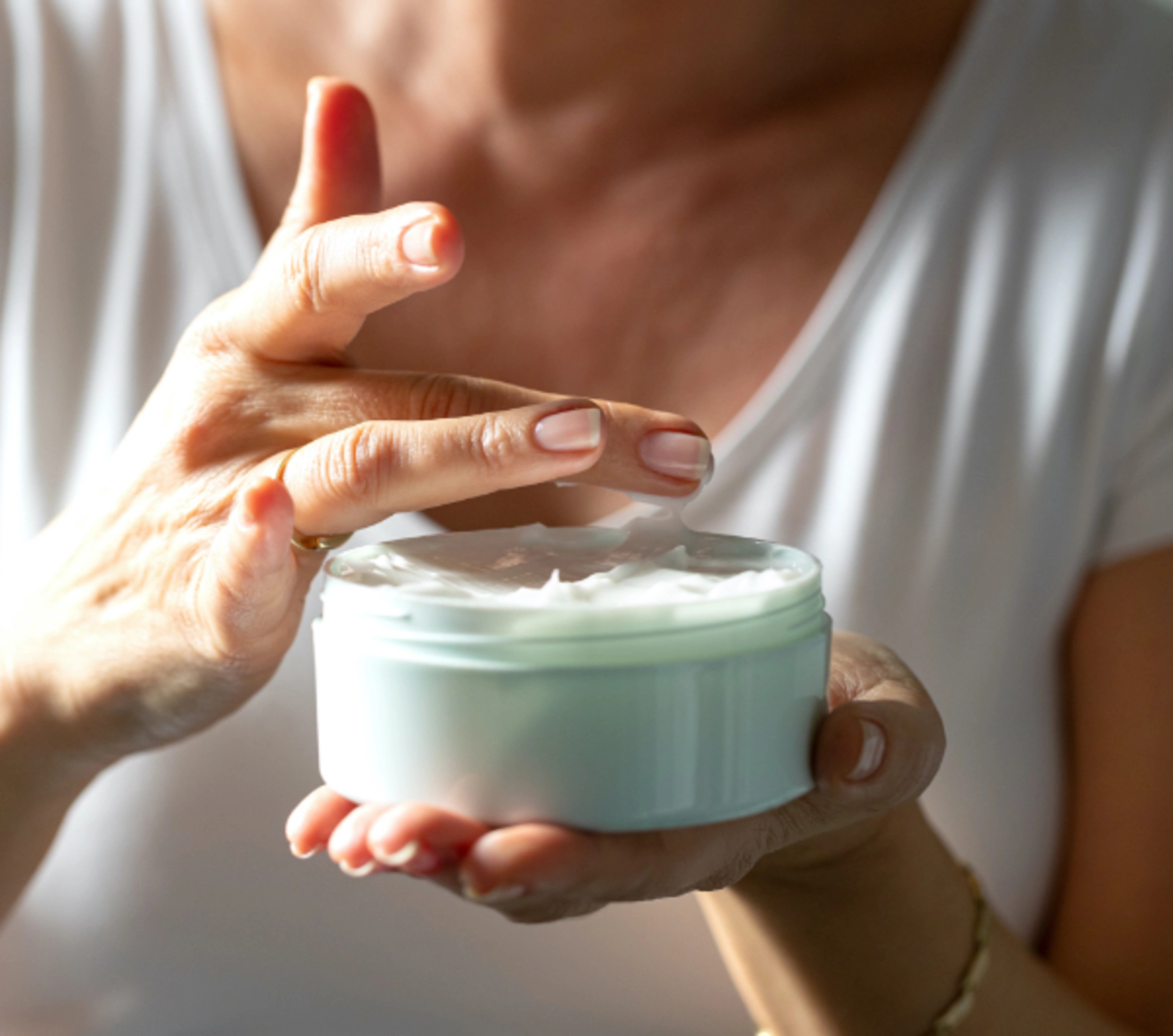 A woman taking lotion out of a light blue container with her fingers.