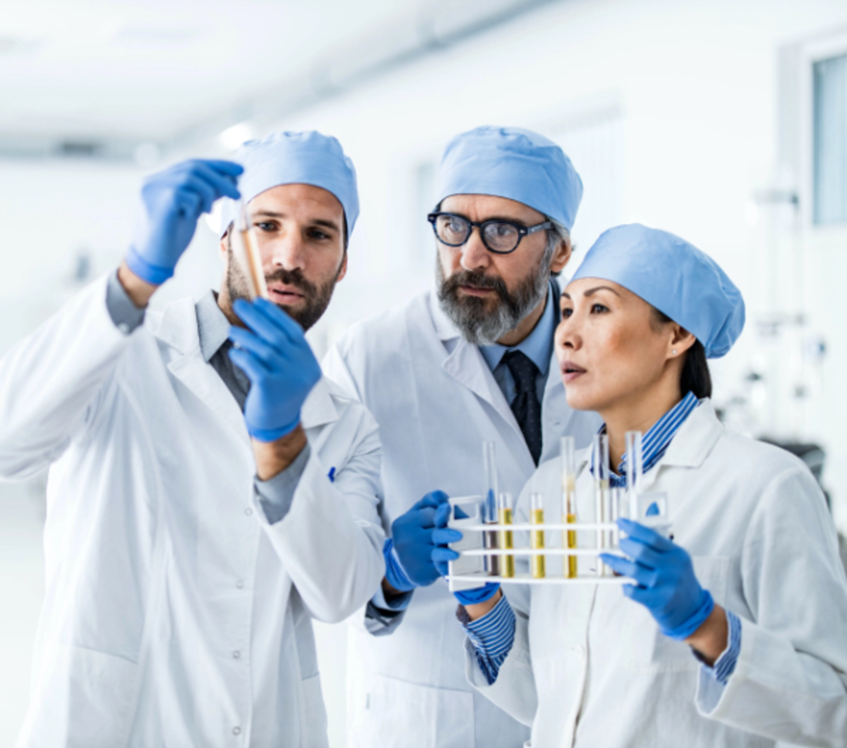 Three scientists look into a test tube at an orange liquid.