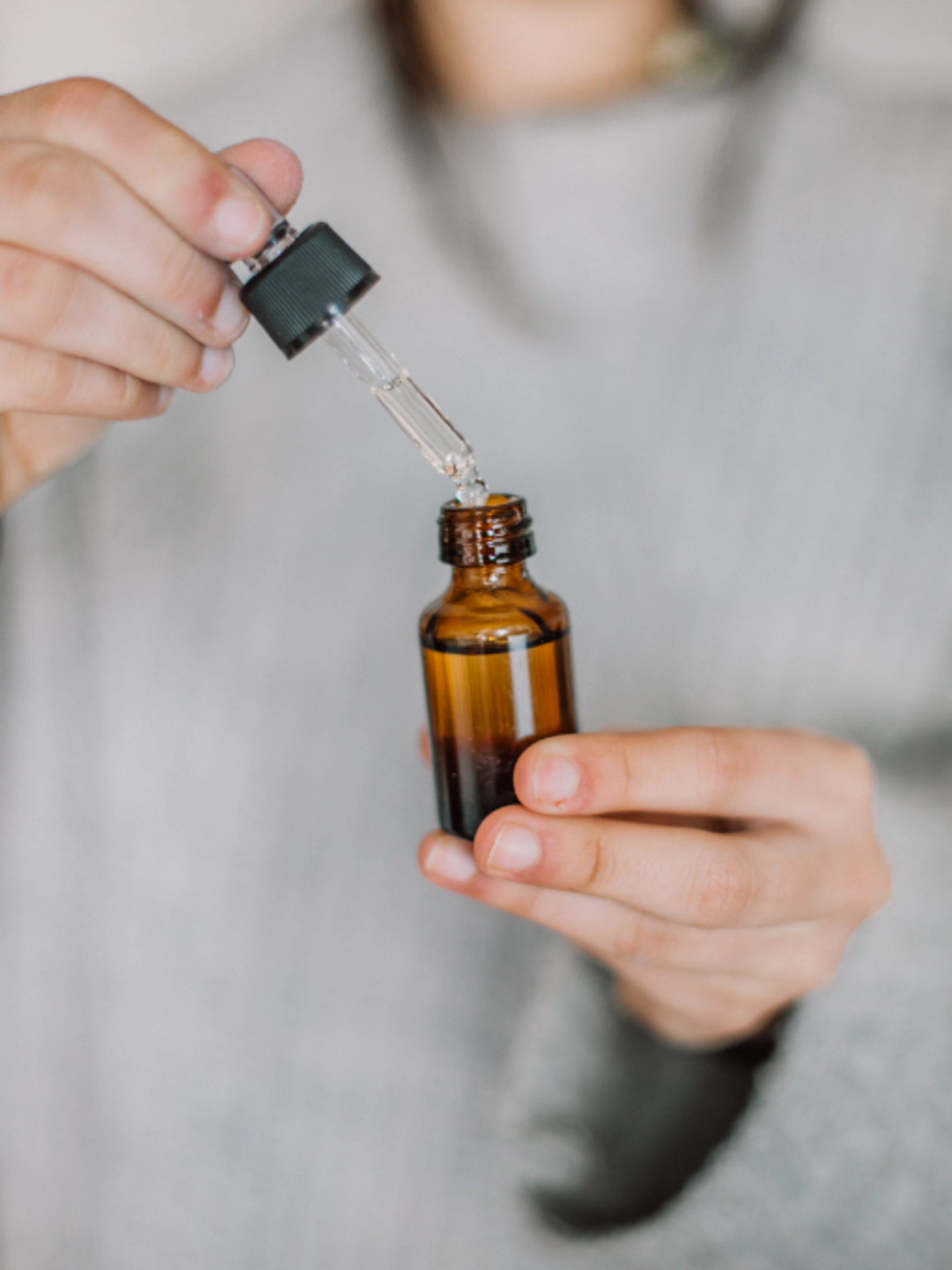 A woman wearing a gray sweater taking a dropper out of a bottle of essential oils.