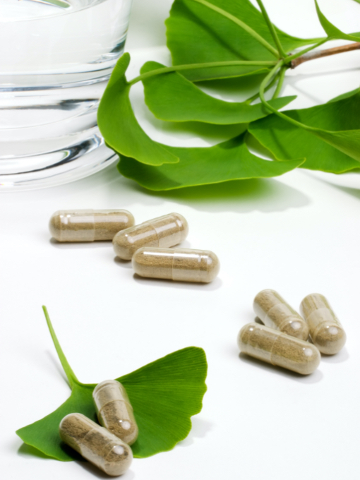 8 capsules filled with herbs lying on a table with green ginkgo biloba leaves.
