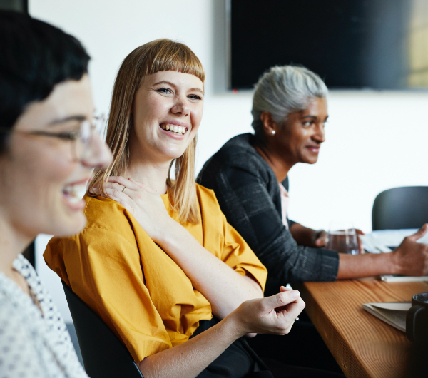 Three women sitting around a conference table smiling and laughing.