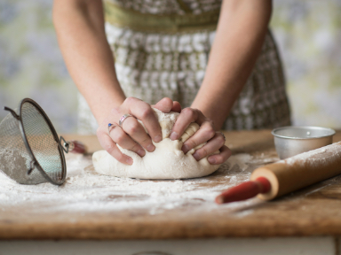 A person's hands kneading bread dough on a table covered in flour.