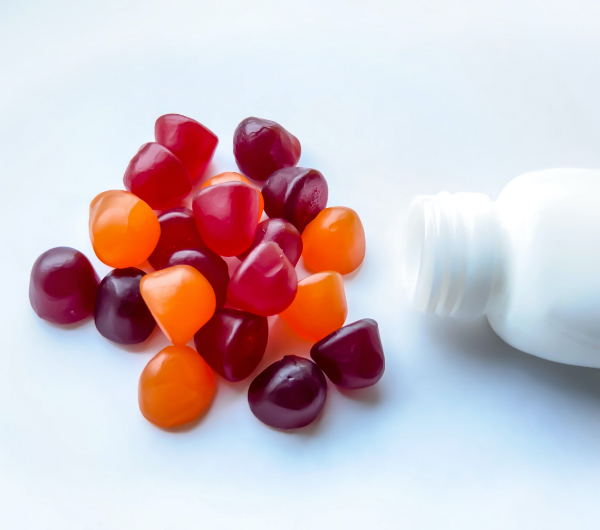 Circular gummies lying on a white table next to a white bottle.