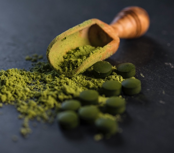 a wooden spoon with green powder and capsules