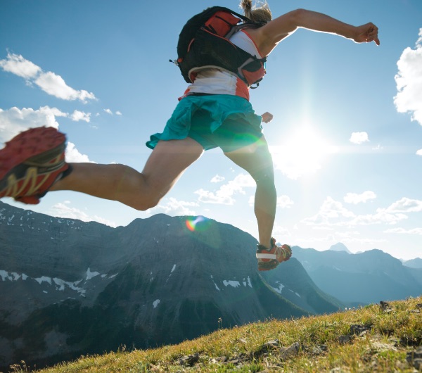 woman in green shorts leaps in front of a mountain