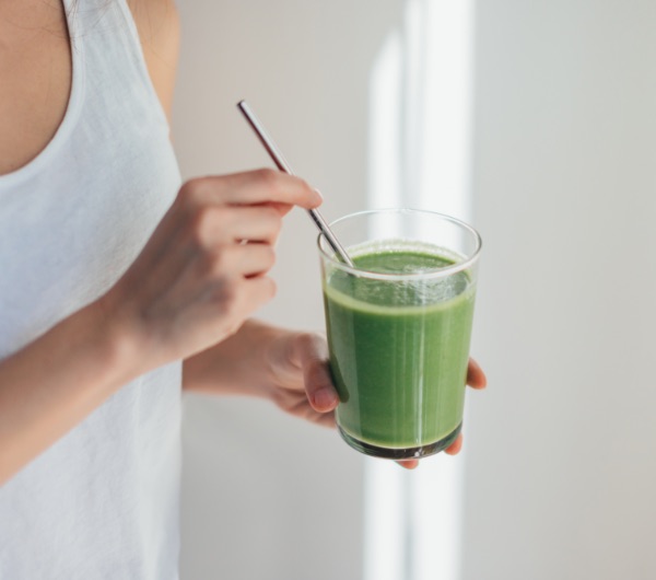 woman holding green beverage in glass cup with metal straw