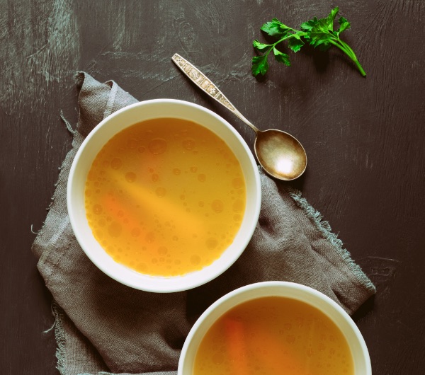 two white bowls of orange broth on a table
