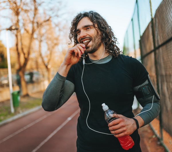 man with long curly hair in a black shirt eats a snack bar after a run