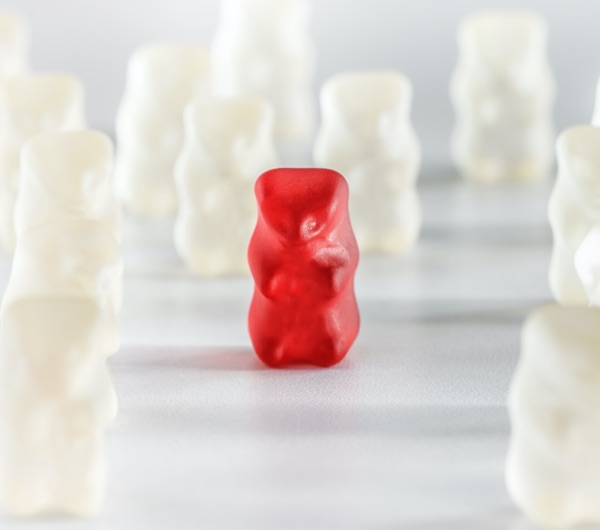 one red gummy bear in the center of several white gummy bears