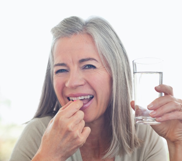 middle aged woman holding a glass of water and putting a tablet in her mouth