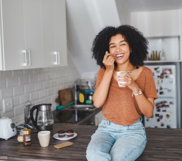 woman sitting on kitchen counter and eating a yogurt