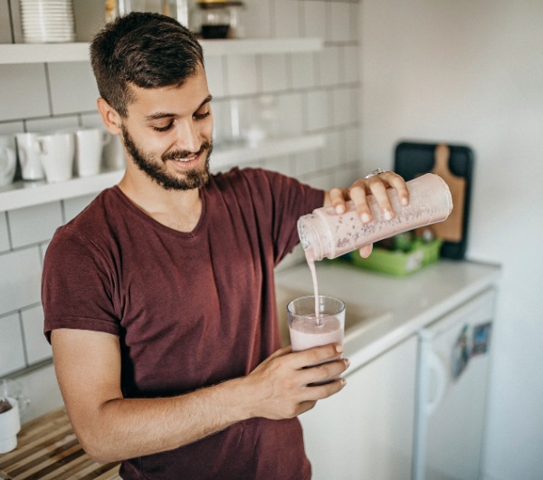 man pouring pink smoothie into glass