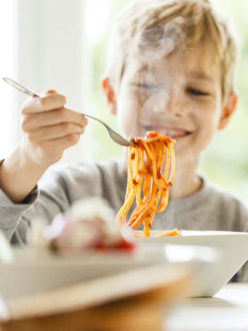 A young boy with blonde hair eating a bowl of spaghetti.