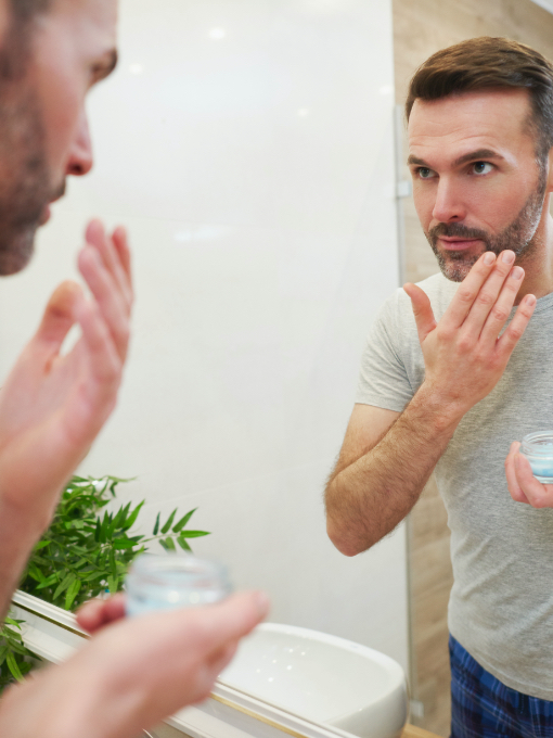 man applying face product in a bathroom mirror