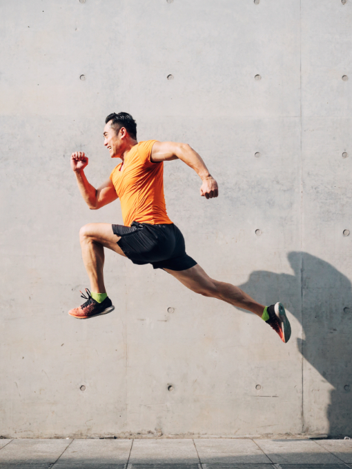 man in orange shirt leaping in front of a concrete wall