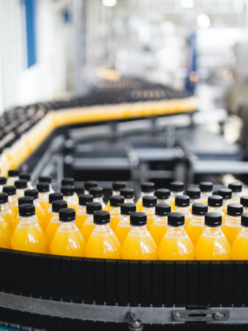 A series of plastic bottles with black caps filled with an orange liquid on a production line.