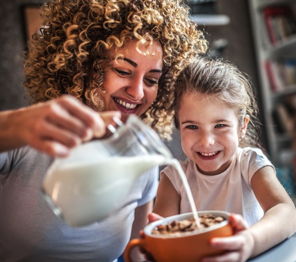 A mother pours milk on to a bowl of cereal for her daughter