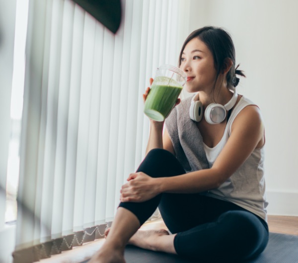 woman with headphones around neck drinking a green smoothie